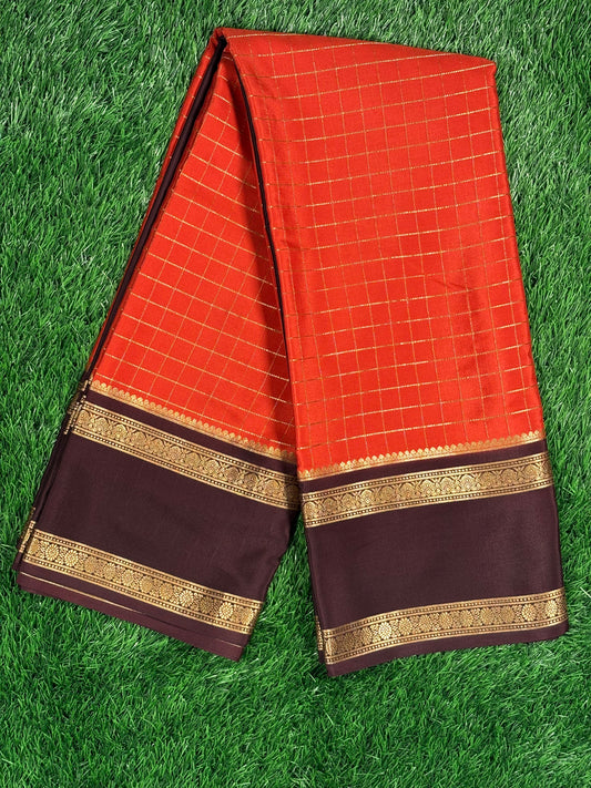 A vibrant burnt orange/brick red body with gold checks, paired with a deep chocolate/coffee brown border and pallu.